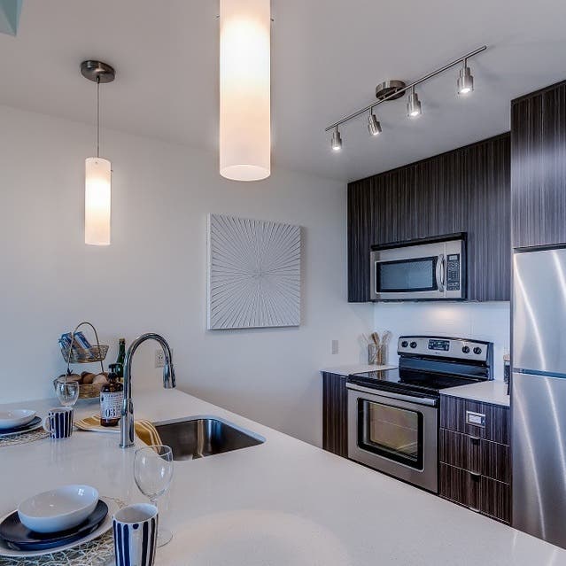 Osprey Apartments - kitchen with large island, dark cabinets, white countertops, and stainless steel appliances
