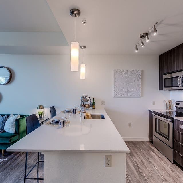 Osprey Apartments - kitchen with large island, dark cabinets, white countertops, and stainless steel appliances