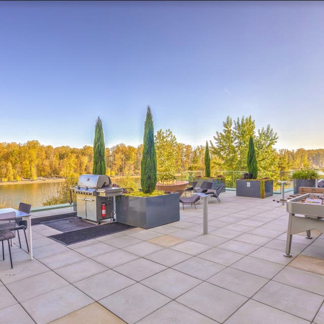 Osprey Apartments - river terrace with grill, outdoor seating, and foosball table